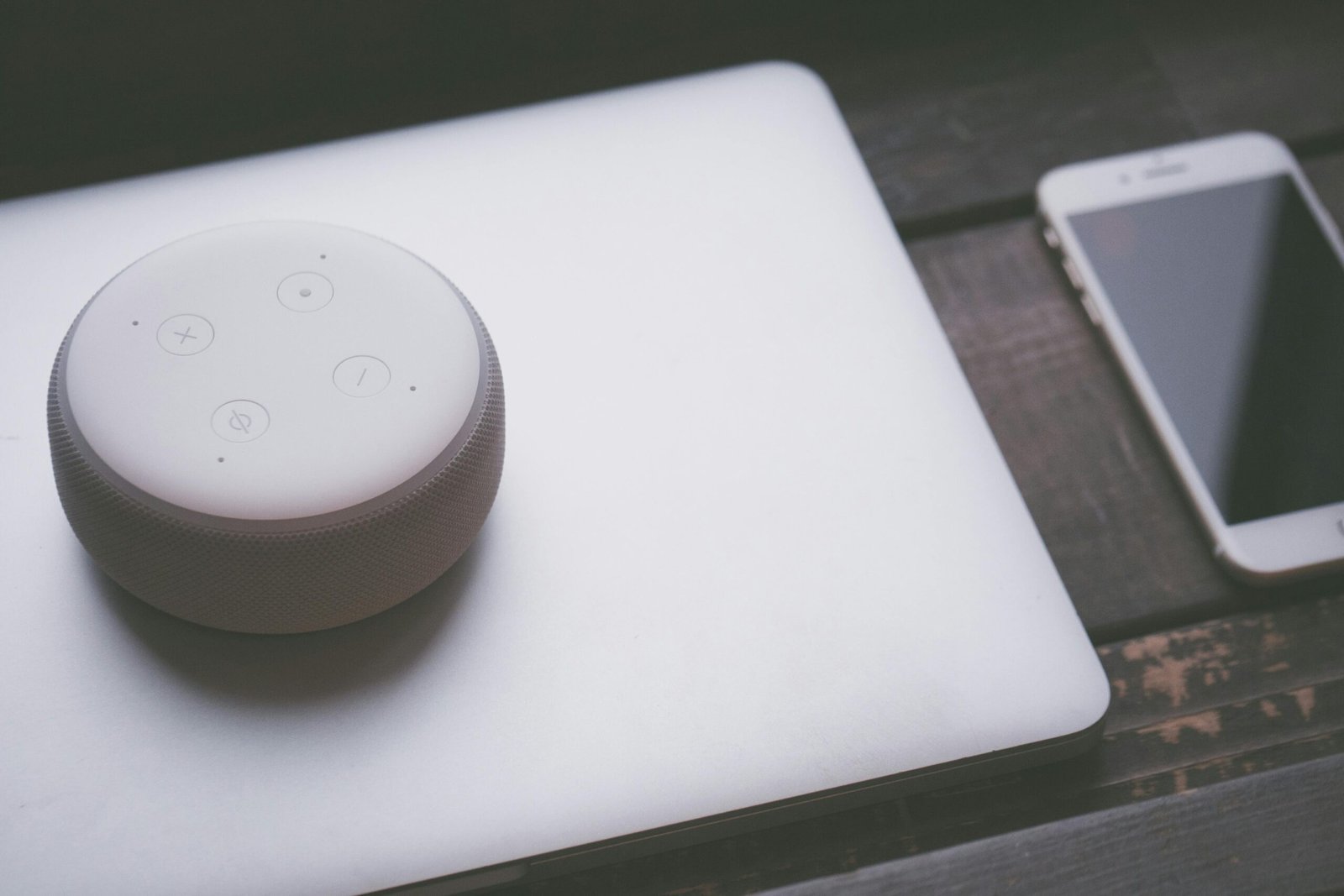 A smart speaker, laptop, and smartphone array representing modern technology lifestyle on a wooden surface.