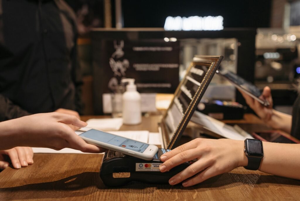 Hands using mobile for contactless payment at café terminal.