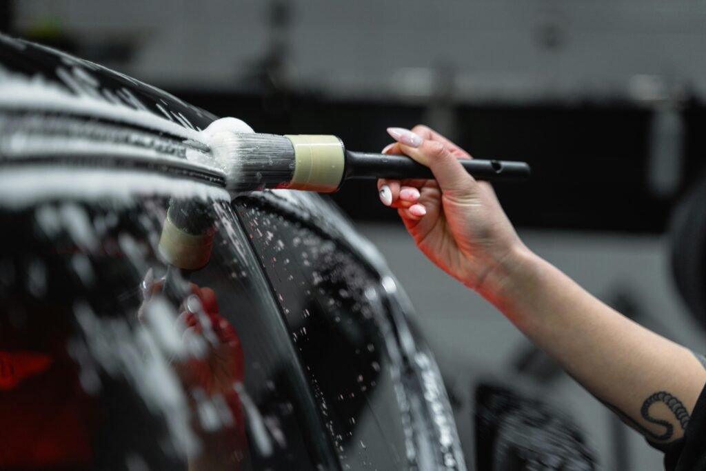 Hand cleaning car exterior with brush and foam in a detailed car wash process.